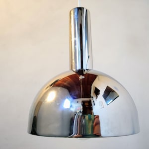 Può includere: Una lampada a sospensione in cromo con un paralume a cupola e uno stelo cilindrico.