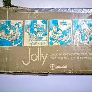Może przedstawiać: Winietkowe pudełko na tacę wielofunkcyjną, nazwaną "Jolly" przez Guzzini. Pudełko zawiera ilustracje tacy używanej w r&oacute;żnych miejscach, w tym sypialni, salonie i pokoju dziecięcym. Tekst na pudełku brzmi "vassoio multiuso - plateau multi-usage multi-purpose tray - mehrzweckplatte".