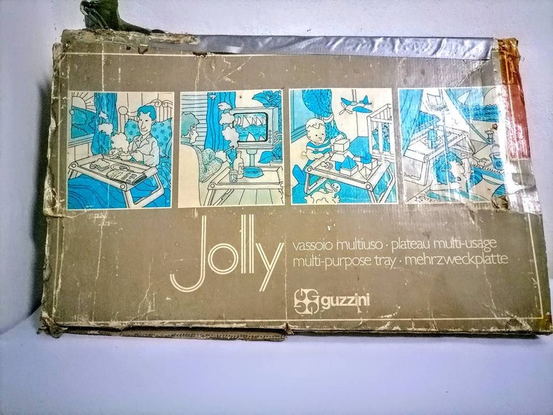 Może przedstawiać: Winietkowe pudełko na tacę wielofunkcyjną, nazwaną "Jolly" przez Guzzini. Pudełko zawiera ilustracje tacy używanej w r&oacute;żnych miejscach, w tym sypialni, salonie i pokoju dziecięcym. Tekst na pudełku brzmi "vassoio multiuso - plateau multi-usage multi-purpose tray - mehrzweckplatte".