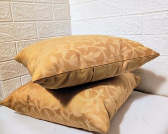 May include: Two gold throw pillows with a floral pattern. The pillows are stacked on top of each other.