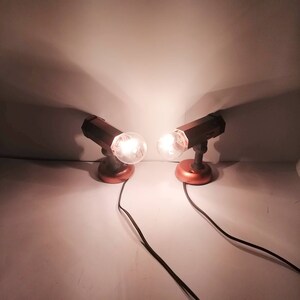 May include: Two brown metal wall-mounted lights with clear glass bulbs turned on, each with a copper base and a black cord.