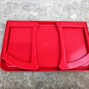 K&ouml;nnte beinhalten: Ein leuchtend roter Laptop-Schreibtisch aus Kunststoff mit zwei klappbaren St&uuml;tzarmen. Der Schreibtisch hat eine rechteckige Form mit abgerundeten Ecken und einem leicht erh&ouml;hten Rand. Die gebogenen St&uuml;tzarm sind mit kreisf&ouml;rmigen Scharnieren an der Basis befestigt.