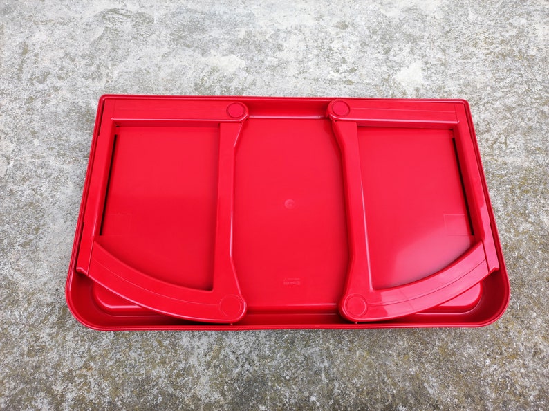K&ouml;nnte beinhalten: Ein leuchtend roter Laptop-Schreibtisch aus Kunststoff mit zwei klappbaren St&uuml;tzarmen. Der Schreibtisch hat eine rechteckige Form mit abgerundeten Ecken und einem leicht erh&ouml;hten Rand. Die gebogenen St&uuml;tzarm sind mit kreisf&ouml;rmigen Scharnieren an der Basis befestigt.