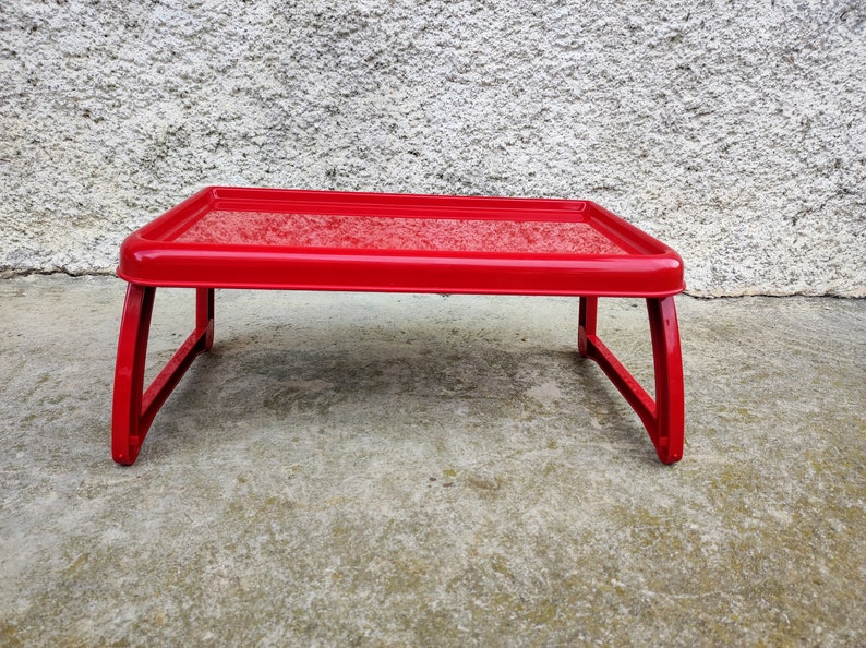 K&ouml;nnte beinhalten: Ein leuchtend roter Laptop-Tisch mit rechteckiger Ablage und gebogenen Beinen. Das Tablett hat erh&ouml;hte Kanten und wird von abgewinkelten Beinen getragen. Der Tisch ist f&uuml;r die Verwendung auf einem Bett oder Sofa konzipiert.