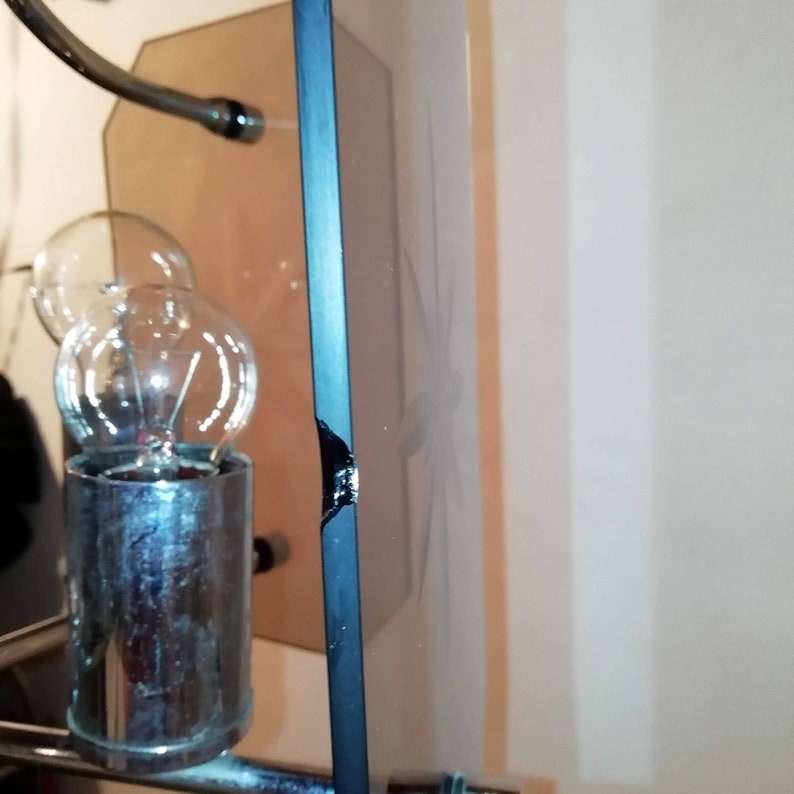 May include: A close-up of a decorative mirror with a black frame. The mirror has a floral design etched into the glass. The frame has a broken section on the edge. A light fixture is visible in the background.