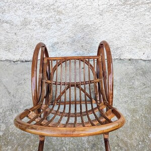 Puede incluir: Una mecedora de mimbre marr&oacute;n con respaldo redondeado y brazos curvos. La silla est&aacute; hecha de rat&aacute;n natural tejido y tiene un acabado liso y pulido.