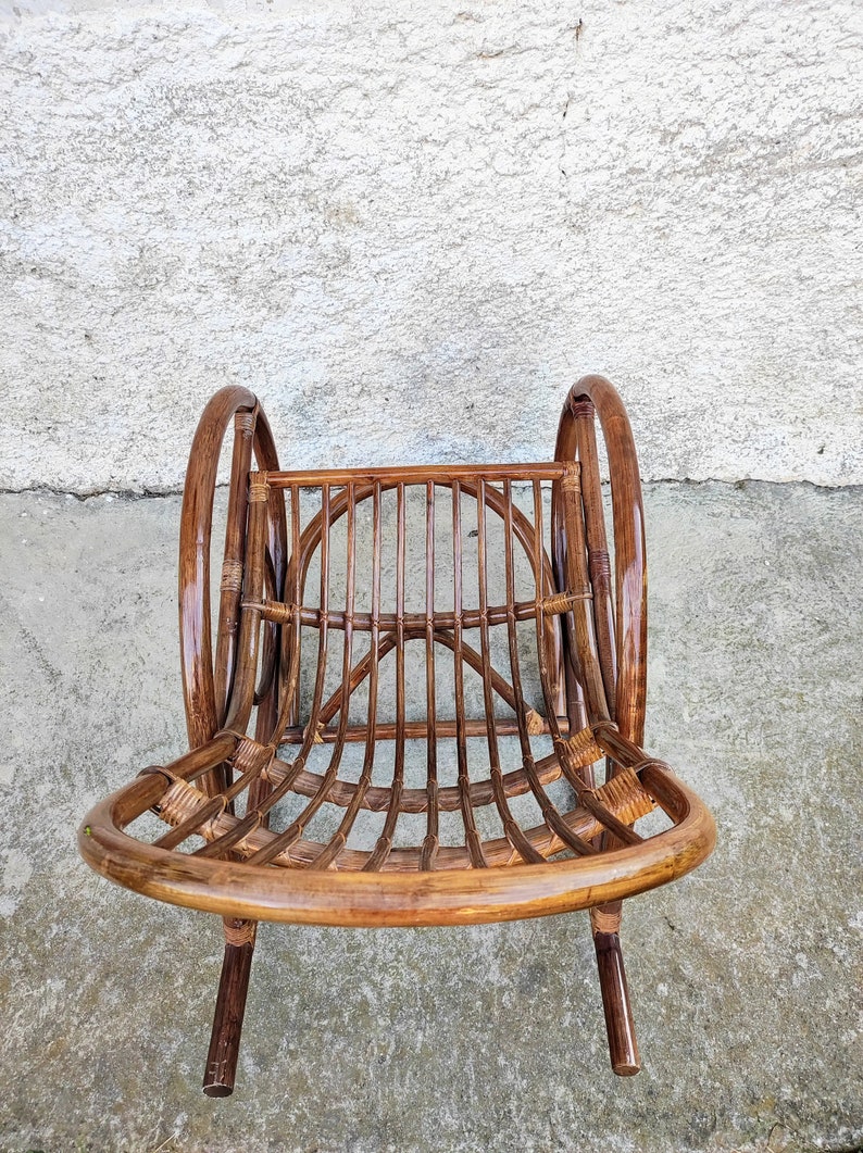 Puede incluir: Una mecedora de mimbre marr&oacute;n con respaldo redondeado y brazos curvos. La silla est&aacute; hecha de rat&aacute;n natural tejido y tiene un acabado liso y pulido.