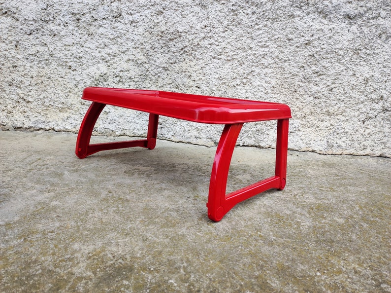K&ouml;nnte beinhalten: Ein leuchtend roter, rechteckiger Scho&szlig;tisch mit gebogenen Beinen. Der Tisch besteht aus einem gl&auml;nzenden Material und ist daf&uuml;r konzipiert, auf dem Scho&szlig; einer Person zu liegen. Der Tisch ist etwa 46 cm lang und 30 cm breit.
