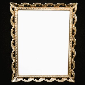 May include: A rectangular picture frame with a metallic gold finish. The frame features an ornate, scalloped edge with swirling, wave-like patterns and a beaded inner border surrounding a plain, white, rectangular center display area.
