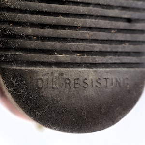 May include: Close-up of a black rubber sole with horizontal grooves. The words "OIL RESISTING" are embossed on the sole. The sole appears to be from a shoe or boot.