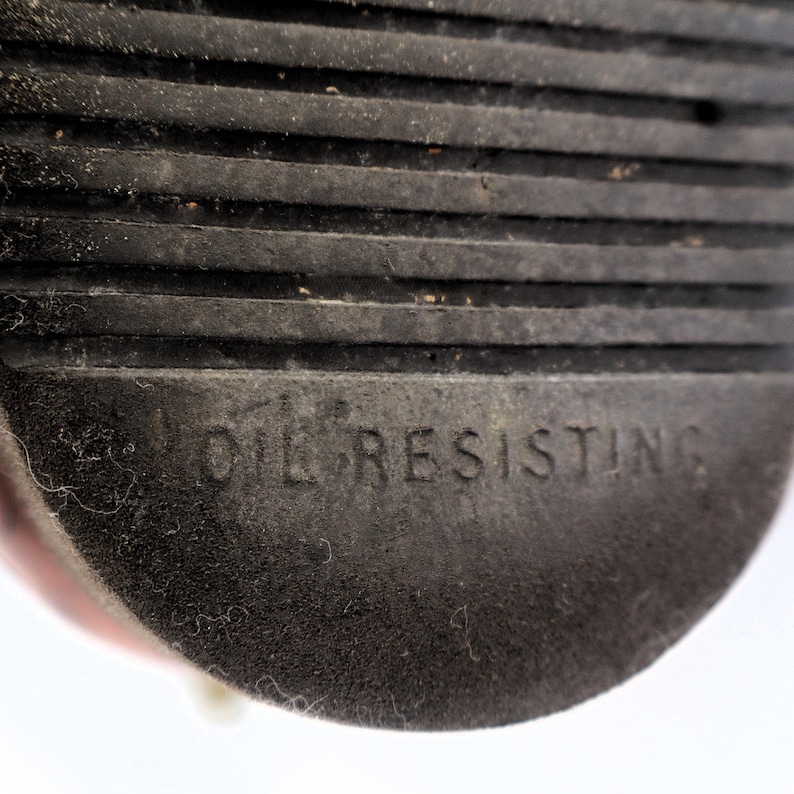May include: Close-up of a black rubber sole with horizontal grooves. The words "OIL RESISTING" are embossed on the sole. The sole appears to be from a shoe or boot.