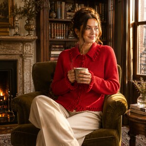 May include: A vibrant red long-sleeved cardigan featuring a collared neckline, button-down front, and decorative fringe trim along the collar, cuffs, and hem, paired with light-colored trousers while holding a ceramic mug.