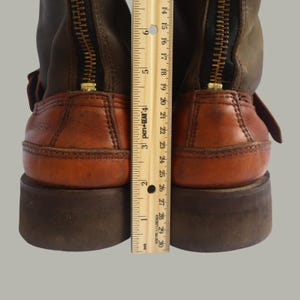 May include: Close-up of two brown and tan leather boots with a zipper up the back. The boots have a brown sole and a ruler is placed next to the boots. The ruler measures approximately 9 inches.