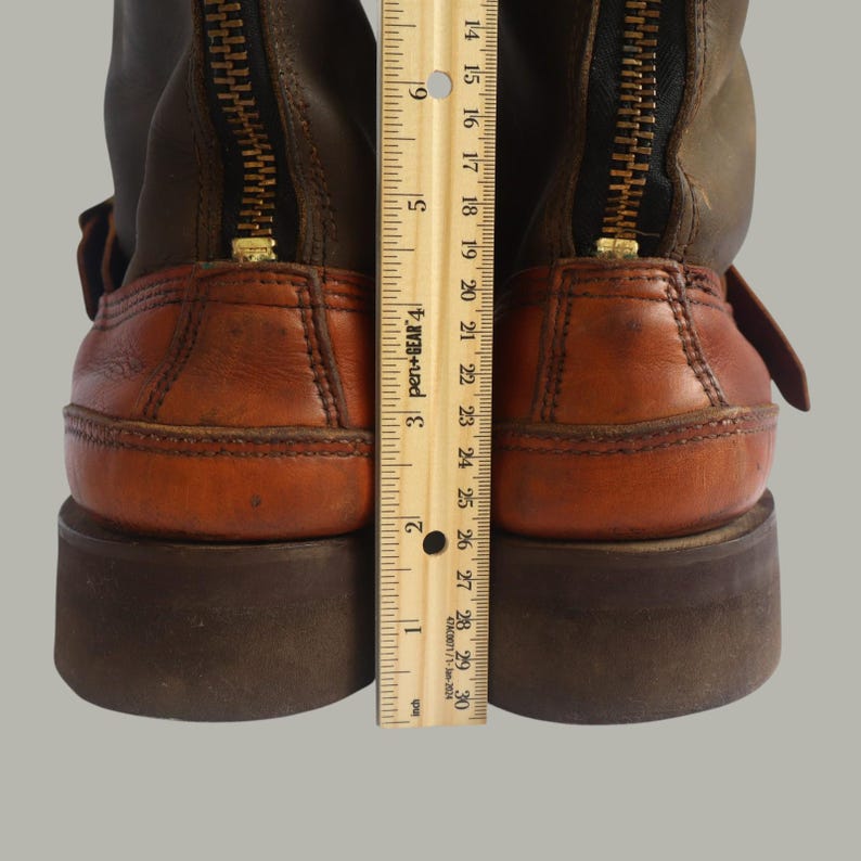 May include: Close-up of two brown and tan leather boots with a zipper up the back. The boots have a brown sole and a ruler is placed next to the boots. The ruler measures approximately 9 inches.