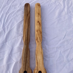 Puede incluir: Dos utensilios de cocina de madera con mango redondeado y un agujero en el extremo. Los utensilios son de madera marrón claro con vetas marrón oscuro.