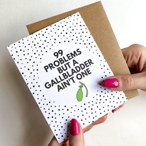 May include: A white card with black polka dots and the text "99 problems but a gallbladder ain't one" with a green olive illustration.