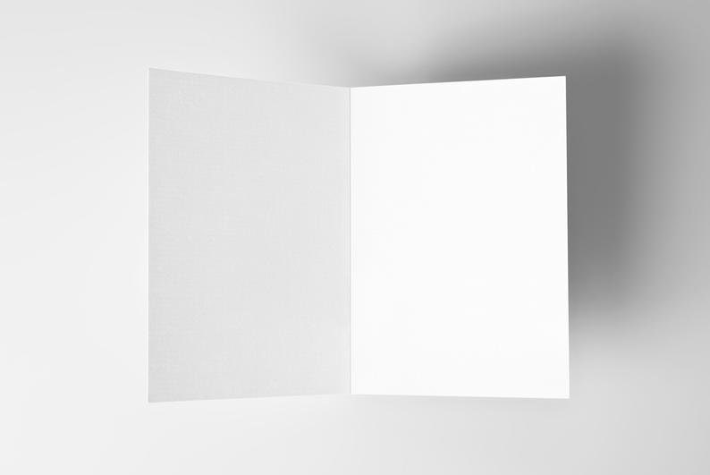 May include: A blank white card folded in half, with a textured surface. The card is sitting on a white background.