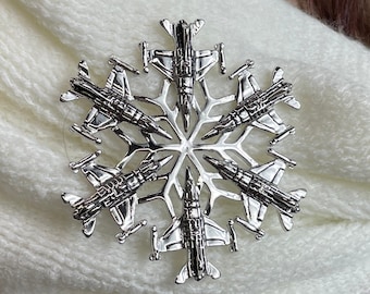 May include: Silver snowflake brooch with six fighter jets forming the points of the snowflake.