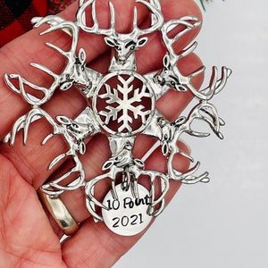 May include: Silver Christmas ornament shaped like a snowflake with six deer antlers surrounding it. The ornament has a small tag hanging from the bottom that says "10 Point 2021".