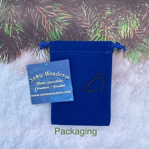 May include: A blue velvet pouch with a white card that says "Snow Wonders Theme Snowflake Ornament/Pendant www.snowwonders.com" and the word "Packaging" printed below the pouch.