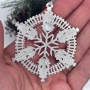 May include: Silver snowflake Christmas ornament with a detailed design of small circles and a fence-like pattern around the edges.