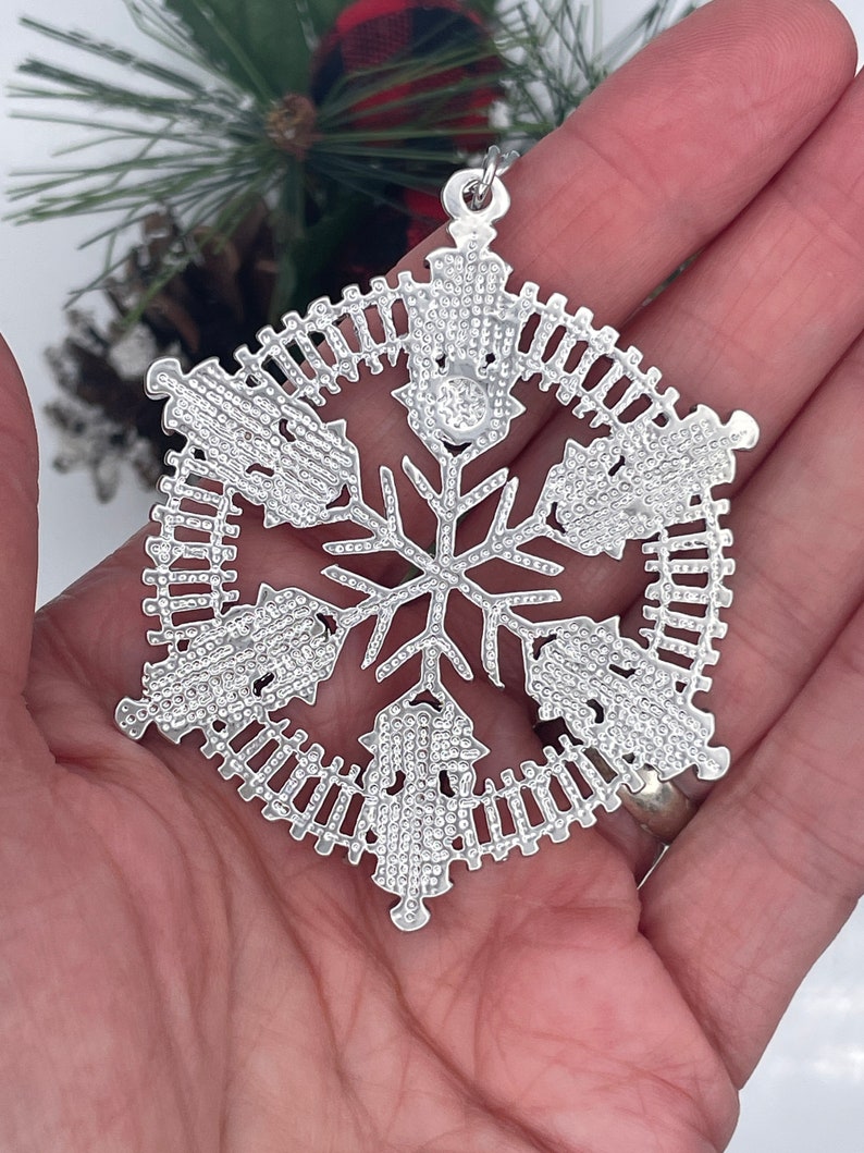 May include: Silver snowflake Christmas ornament with a detailed design of small circles and a fence-like pattern around the edges.