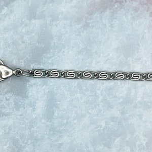 May include: A silver chain necklace with a lobster clasp closure. The chain is made of small, linked ovals.