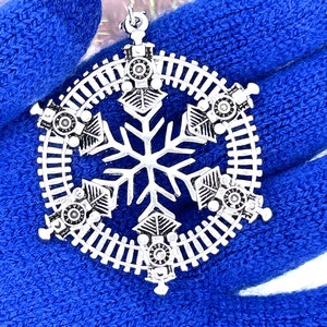 May include: Silver snowflake Christmas ornament with a train track design and six small train engines around the snowflake.