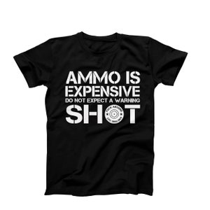 May include: Black t-shirt with white text that reads "AMMO IS EXPENSIVE DO NOT EXPECT A WARNING SHOT." The word "SHOT" has a target graphic in the center. The shirt is a crew neck.