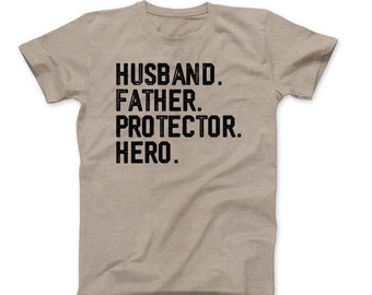 May include: A beige t-shirt featuring the text "HUSBAND. FATHER. PROTECTOR. HERO." in bold, black capital letters. The shirt is made of a soft material and has short sleeves.