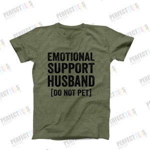 Puede incluir: Una camiseta verde con el texto "Emotional Support Husband [Do Not Pet]" impreso en negro.