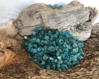 May include: A pile of teal blue aquamarine gemstone chips on a brown fur surface. The chips are various sizes and shapes.