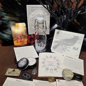 May include: A collection of witchy items including a bottle of moon water, a candle, a Septarian stone, a Green Banded Onyx stone, a Shungite stone, a tarot card, an incense, and a calendar with the astrological signs.