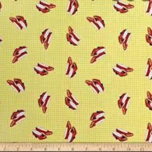 May include: Yellow fabric with a small checkered pattern featuring a repeating design of bacon strips. The bacon is red and white, and the fabric has a ruler along the bottom edge.
