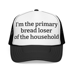 May include: A black and white trucker hat featuring a white front panel with the black text "I'm the primary bread loser of the household" printed in a bold font. The hat includes a black brim and black mesh side and back panels.