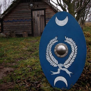 Może przedstawiać: Niebieska tarcza z białym wieńcem laurowym i dwoma półksiężycami. Tarcza ma srebrne metalowe centrum.