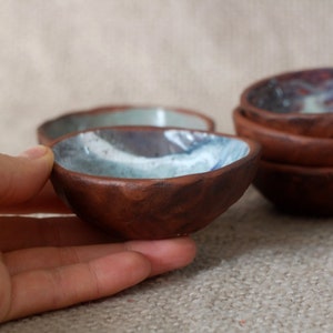 May include: Set of small, rustic brown ceramic bowls with a blue and white glaze. The bowls are handmade and have a unique, textured surface.