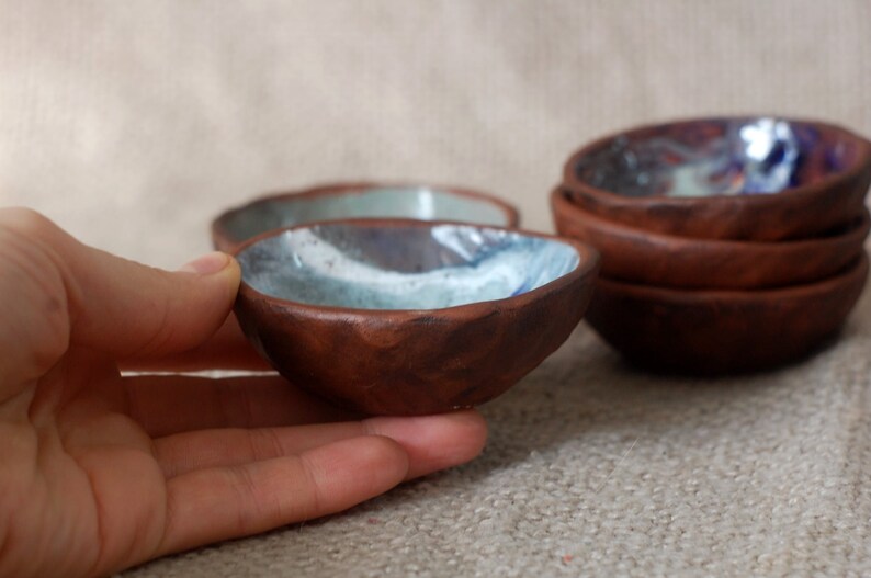May include: Set of small, rustic brown ceramic bowls with a blue and white glaze. The bowls are handmade and have a unique, textured surface.