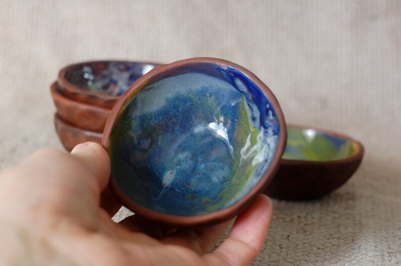 May include: Set of four small ceramic bowls with a blue, green, and white glaze. The bowls are handmade and have a rustic, earthy feel.