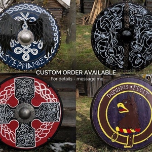 May include: Four round wooden shields with different designs. The shields are painted with intricate patterns and designs, including a black bird with wings spread, a Celtic knot design, a cross with a Celtic knot design, and a purple and brown design with a bird and the text "DOMINUS FECIT".