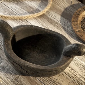 May include: A dark wooden bowl with two bird-shaped handles. The bowl is carved with intricate details and has a rustic appearance.