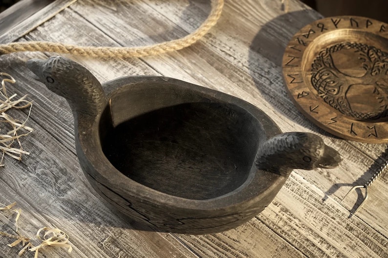 May include: A dark wooden bowl with two bird-shaped handles. The bowl is carved with intricate details and has a rustic appearance.