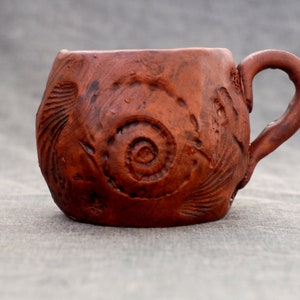 Puede incluir: Una taza de cerámica marrón con un diseño texturizado en espiral. La taza tiene un cuerpo redondeado y un asa.