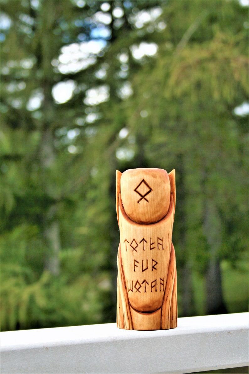 May include: A wooden totem carved with runes and the words "Totem Fur Wotan". The totem is a light brown color and has a smooth finish.