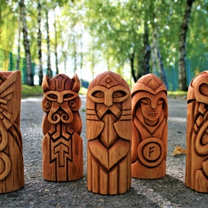 May include: Five wooden carvings of Norse gods and goddesses, each with intricate details and a unique design. The carvings are made of a light brown wood and are arranged in a row on a gray surface.