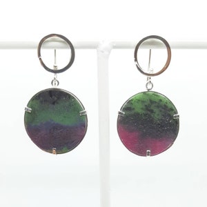 Op de afbeelding: Een paar zilveren oorbellen met ronde groene, paarse en roze edelsteen druppels. De oorbellen hebben een zilveren ring aan de bovenkant.