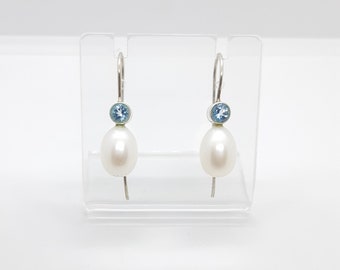 May include: A pair of silver dangle earrings with a white pearl and a light blue gemstone on each earring.