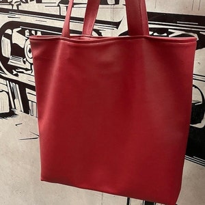 May include: A solid red tote bag with matching handles. The bag is made of a smooth material and has a rectangular shape. The background features a black and white graphic design.