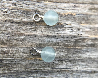 May include: Two silver bead caps with light blue gemstone beads. The beads are round and have a smooth, polished finish.