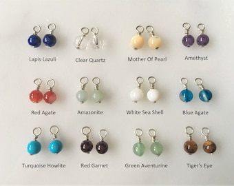 May include: Twelve pairs of gemstone beads with silver wire loops. The beads are in various colors, including blue, clear, white, purple, red, green, turquoise, and brown.